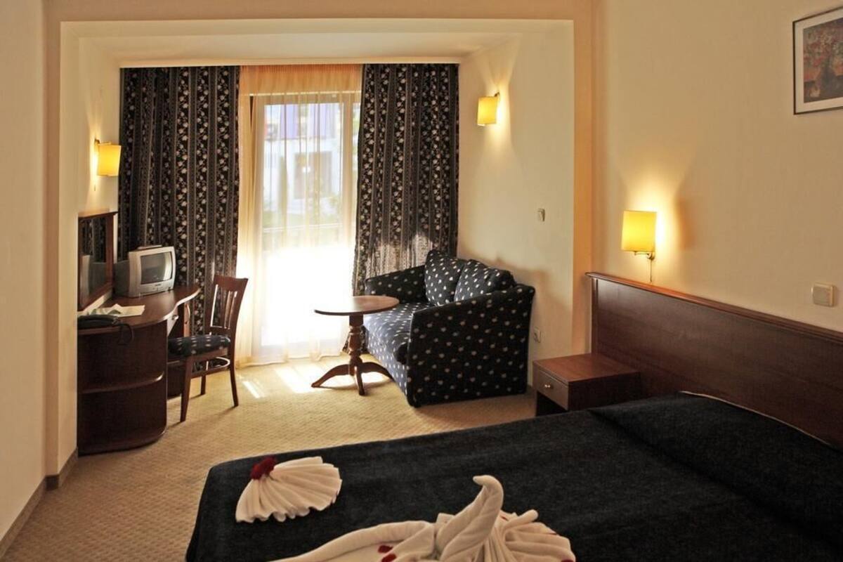 A hotel room with a bed, a desk with a television, a chair, a small table, and curtains.