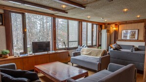A cozy living room with a fireplace, large windows, and comfortable seating. - Powder Temple (Hakuba)