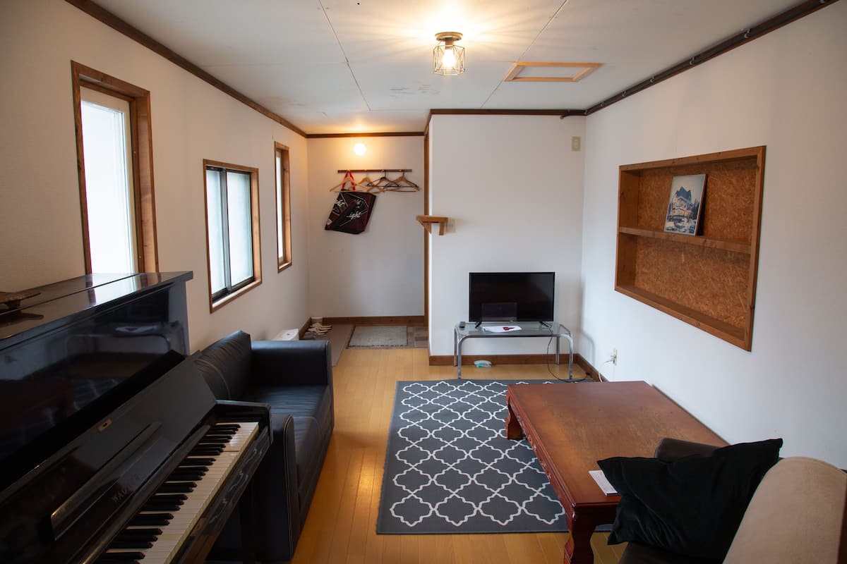 Uma sala de estar com um piano, uma televisão, um sofá e uma mesa de madeira.