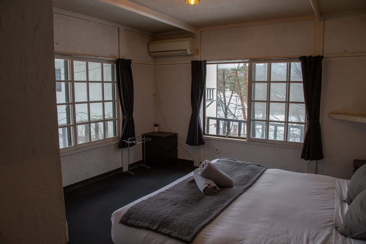 Quarto de hotel com cama, mesa de cabeceira pequena, ar condicionado e janela com cortinas.