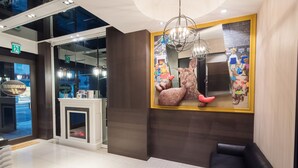 A modern lobby with a reception desk, a large mirror with a colorful mural, a black leather sofa, and a chandelier. - Sunrise Business Hotel Ximen (Taipei)