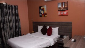 A hotel room with a bed, a nightstand, a desk, and two paintings on the wall. - House 46 (Lagos)