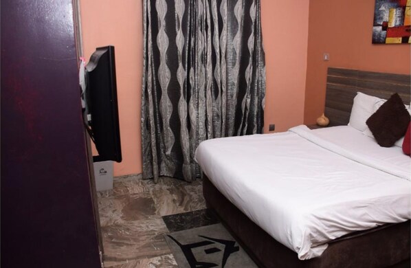Un dormitorio con cama, televisor, cortinas estampadas y una obra de arte en la pared.