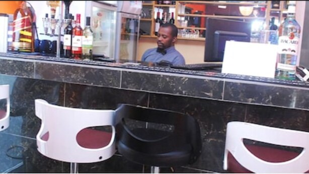 A bar area with a counter, several chairs, and a variety of bottles in the background. - House 46 (Lagos)