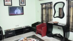 A living room with a TV, framed pictures, a sofa, a red chair, and a console table. - House 46 (Lagos)