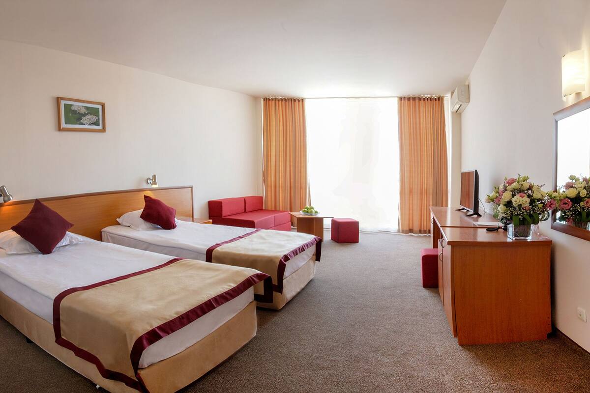 A hotel room with two beds, a desk, a chair, a sofa, and a TV.