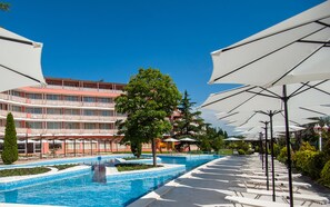 A swimming pool with lounge chairs and umbrellas, surrounded by a building with balconies.