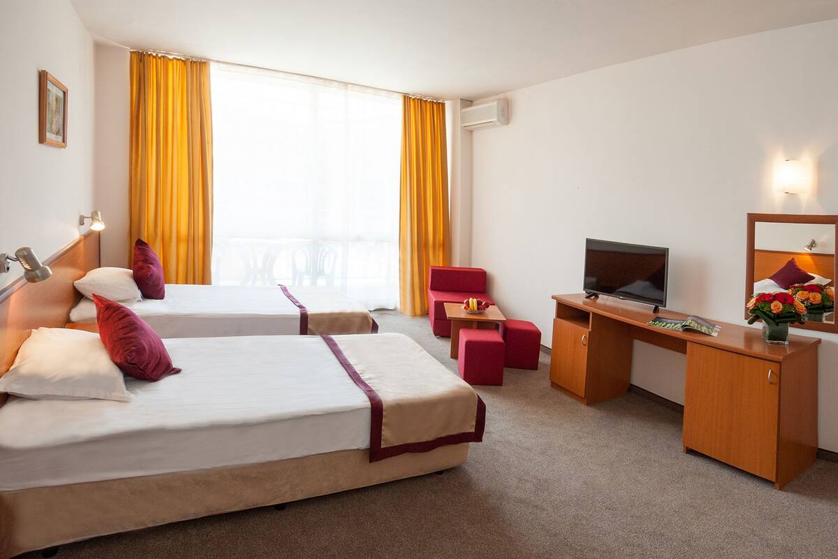 A hotel room with two beds, a desk, a TV, and a mirror.