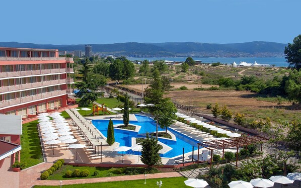 A hotel with a pool, outdoor seating, and a view of the sea and mountains.