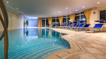 An indoor swimming pool with blue lounge chairs and yellow curtains.