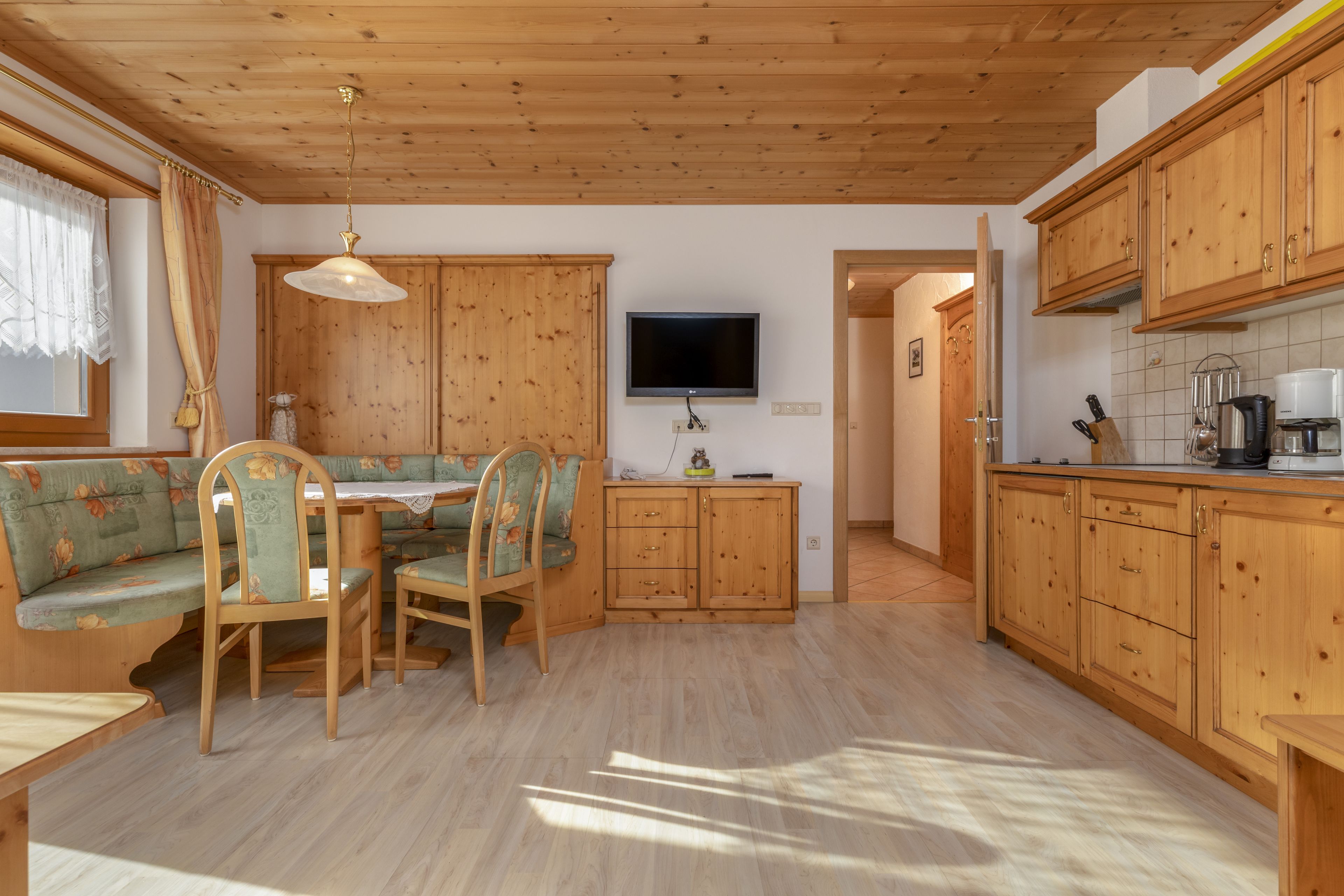 A cozy kitchen with wooden cabinets, a dining table with chairs, and a TV mounted on the wall.