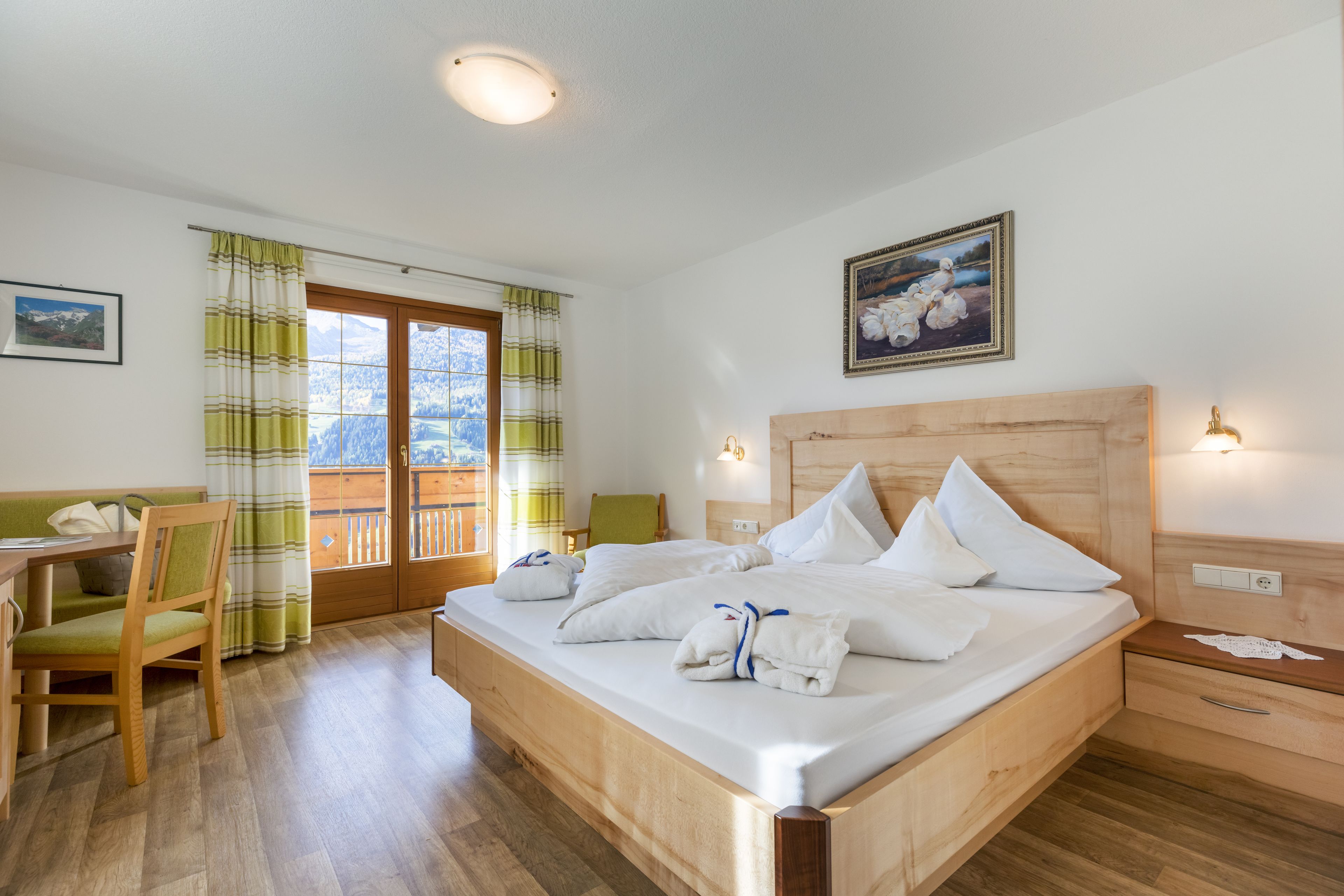Ett hotellrum med en säng i trä, ett skrivbord, en stol och en balkong med gardiner.