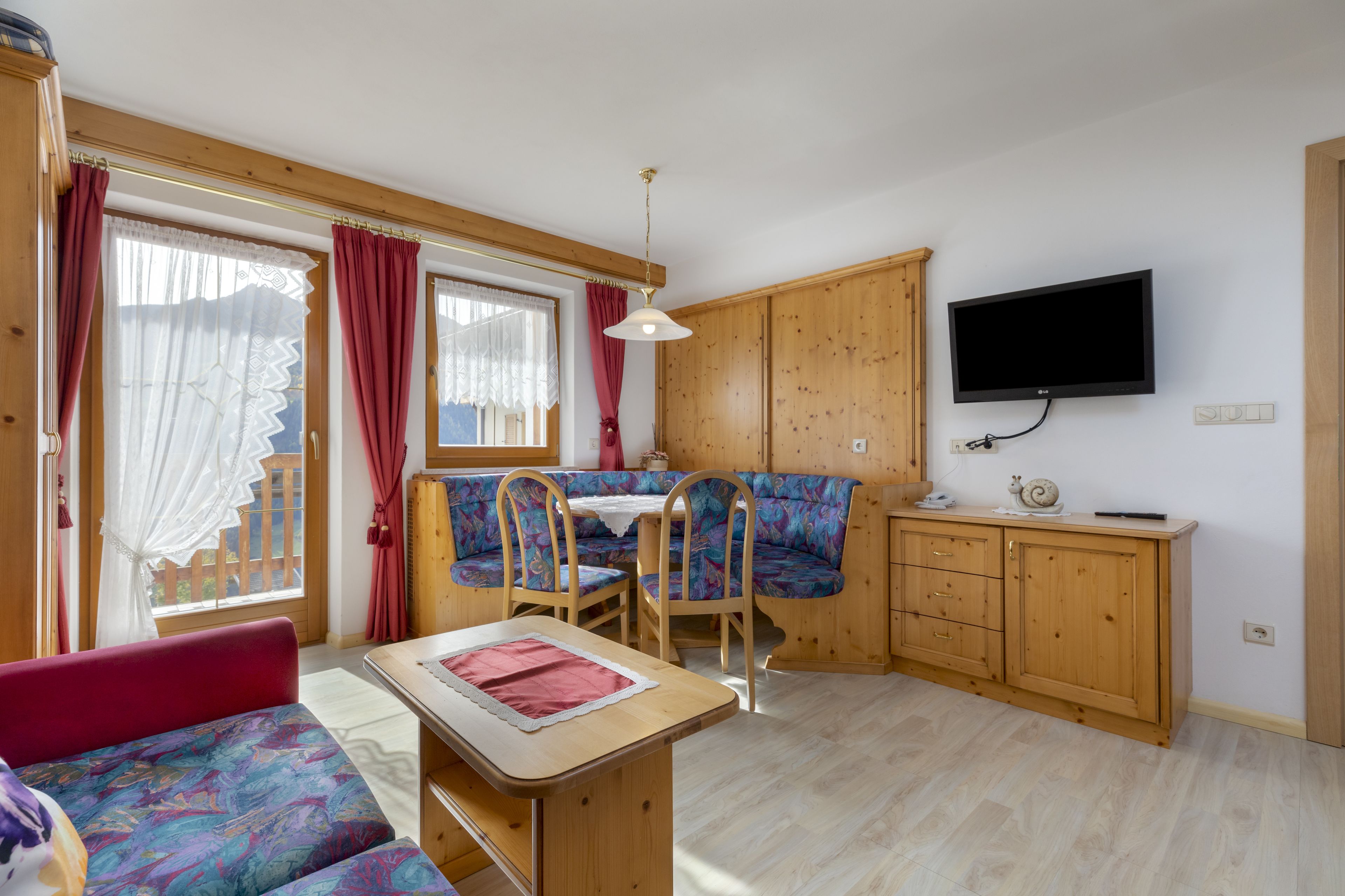 A cozy room with a wooden dining table, a sofa, and a television mounted on the wall.