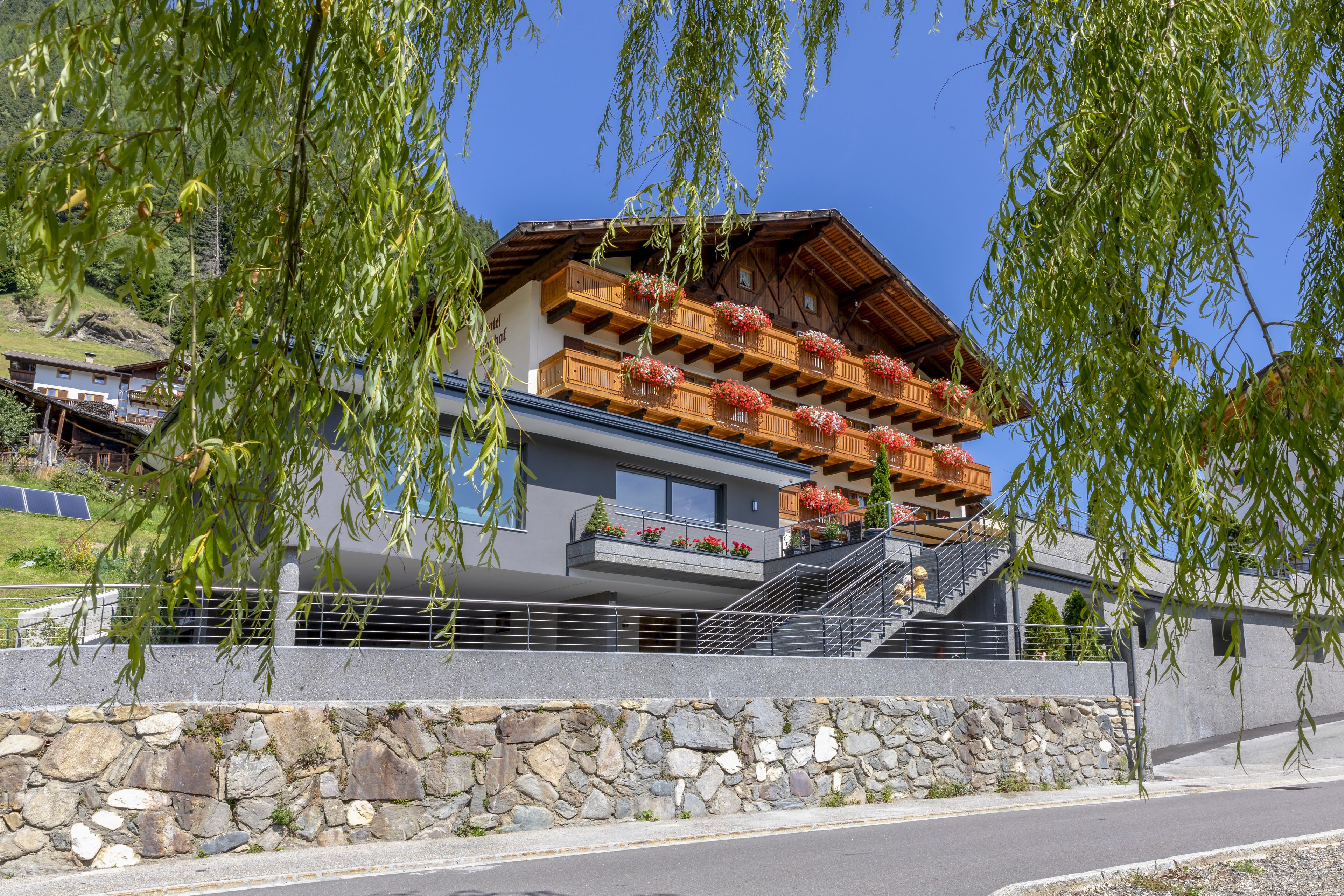 A modern hotel with a stone facade, wooden balconies with flower boxes, and a clear view of the surrounding landscape.