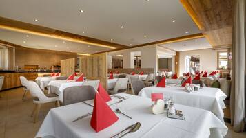 Un restaurant amb diverses taules preparades per dinar, amb teles de taula blanques, serretes vermelles i coberts.