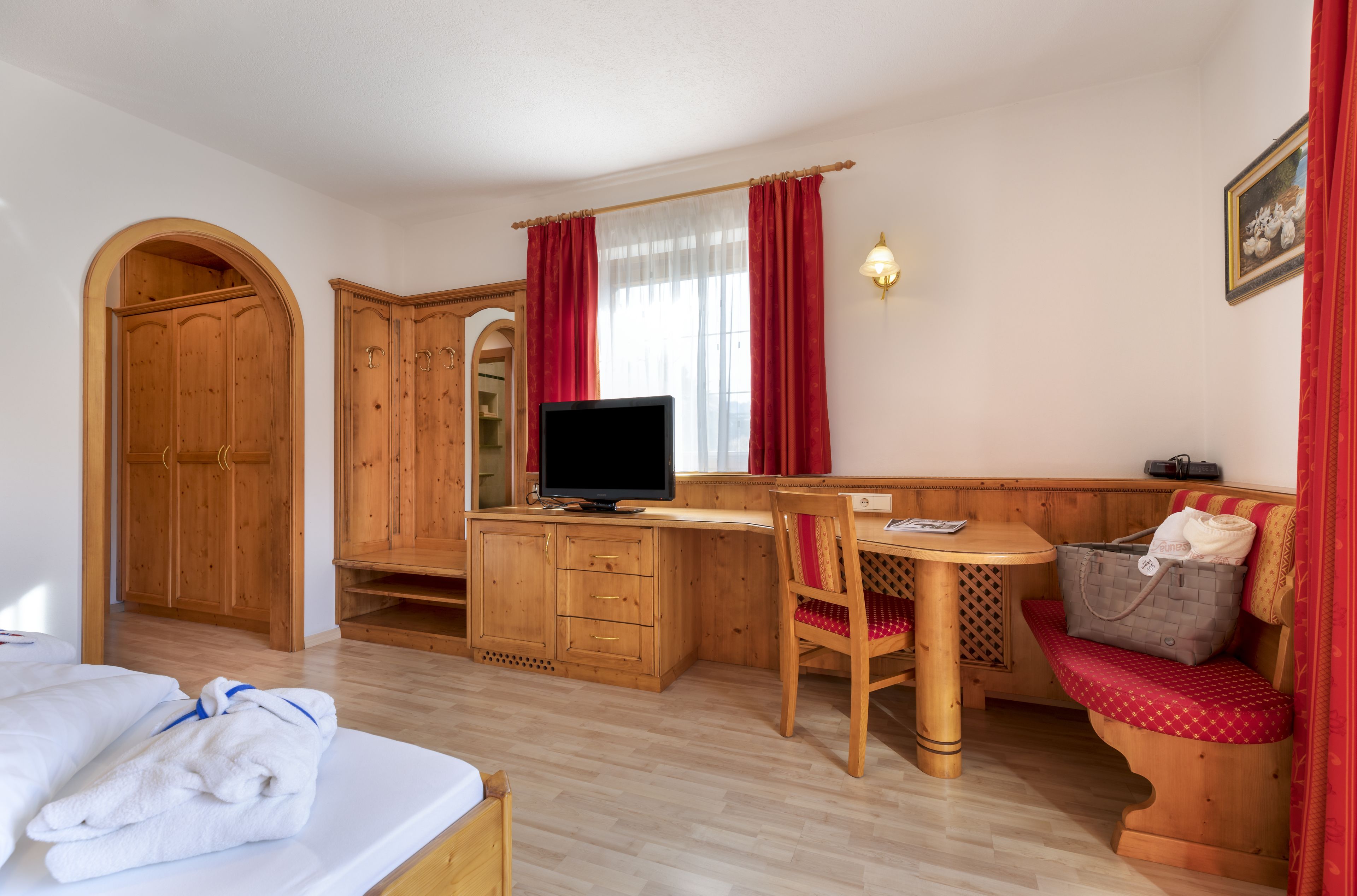 A wooden room with a bed, a desk with a computer, a chair, a bench, and a wardrobe.