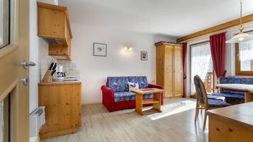 A compact kitchen with wooden cabinets, a red sofa, a small dining table, and a chair.