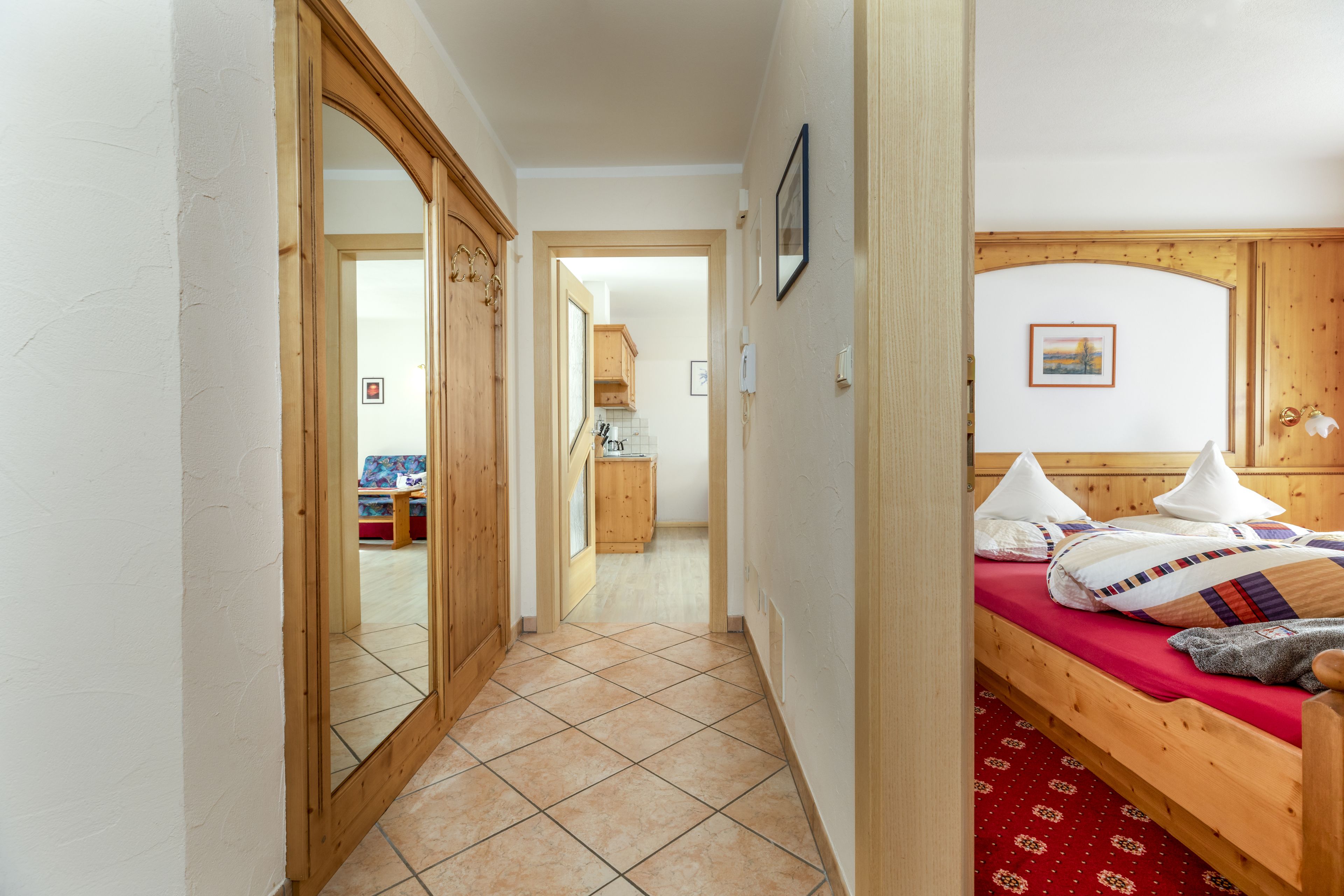 A narrow hallway leading to a bedroom with a wooden bed, a red patterned rug, and a wooden wardrobe.