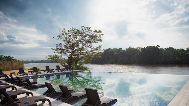 Zona junto a la piscina con sillones de descanso y vistas a un lago.