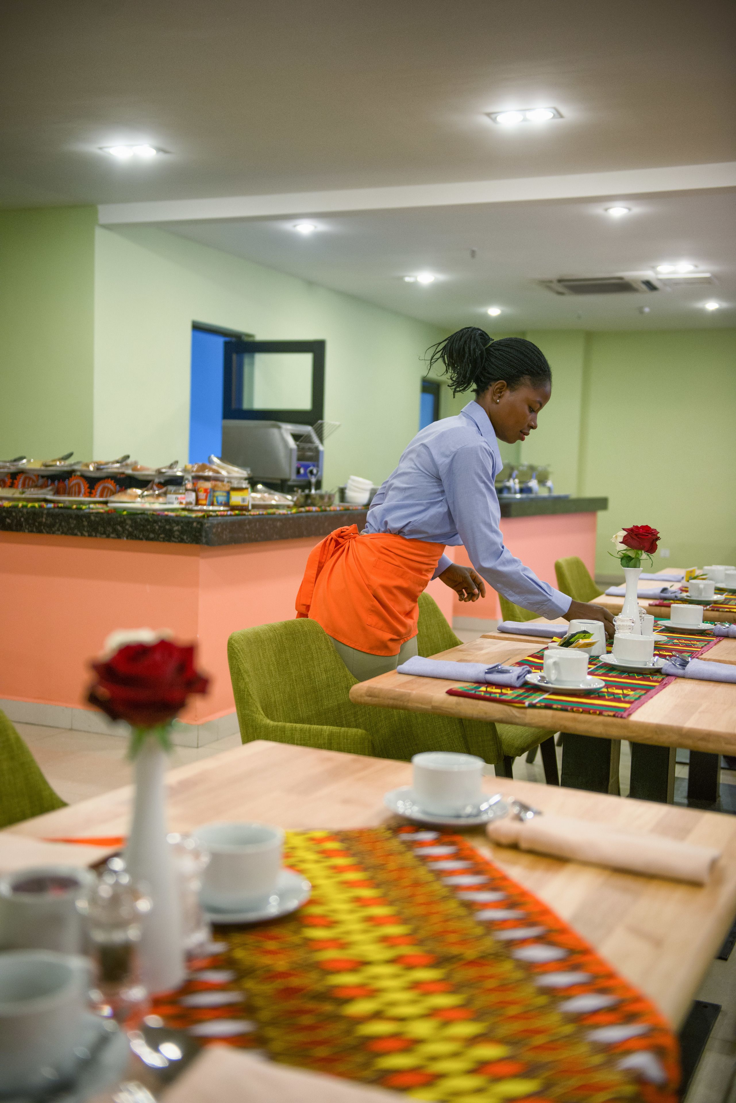 Un restaurante con barra, mesas dispuestas con vajilla blanca y un camarero con delantal naranja.