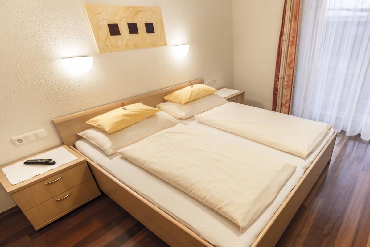 A double bed with two pillows, a bedside table with a remote control, and a wooden nightstand.