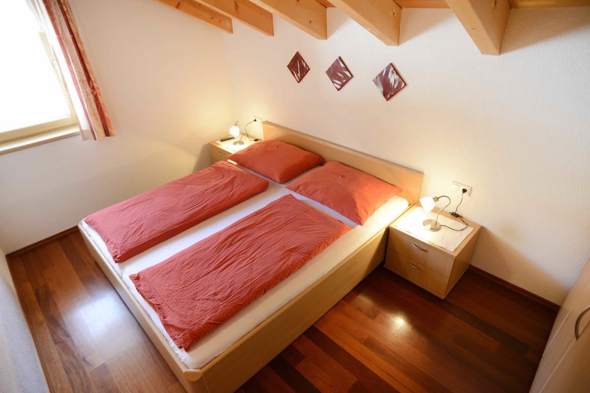 A double bed with a wooden frame, two bedside tables with lamps, and a window with curtains.