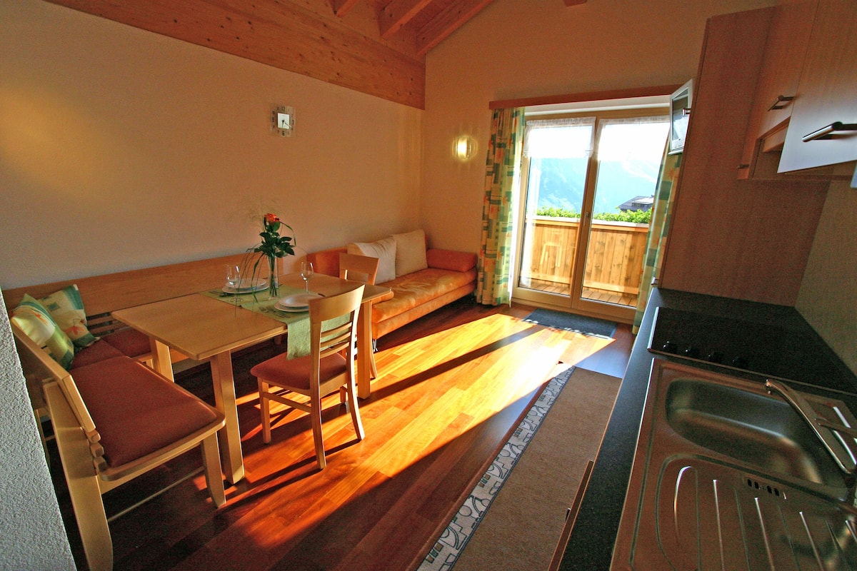 A cozy room with a wooden dining table, chairs, a sofa, and a kitchen area with a sink.