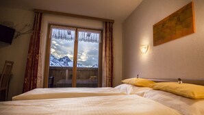 Un dormitorio con un amplio ventanal que ofrece vistas a la montaña, una cama con ropa blanca y una lámpara fijada a la pared.