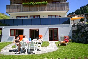 A two-story building with a stone pathway leading to a patio area. - Haus Rothorn (Schroecken)