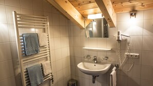 Un baño con lavamanos blanco, un espejo, toalleros con toallas y techo de madera.