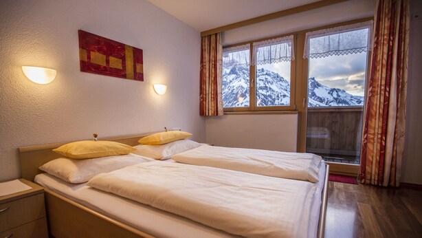 Un dormitorio con dos camas, una ventana con vistas a la montaña y una lámpara fijada a la pared.