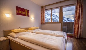 A bedroom with two beds, a window with a mountain view, and a wall-mounted light fixture. - Haus Rothorn (Schroecken)