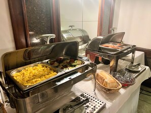A buffet with various food options including scrambled eggs, vegetables, and bread.