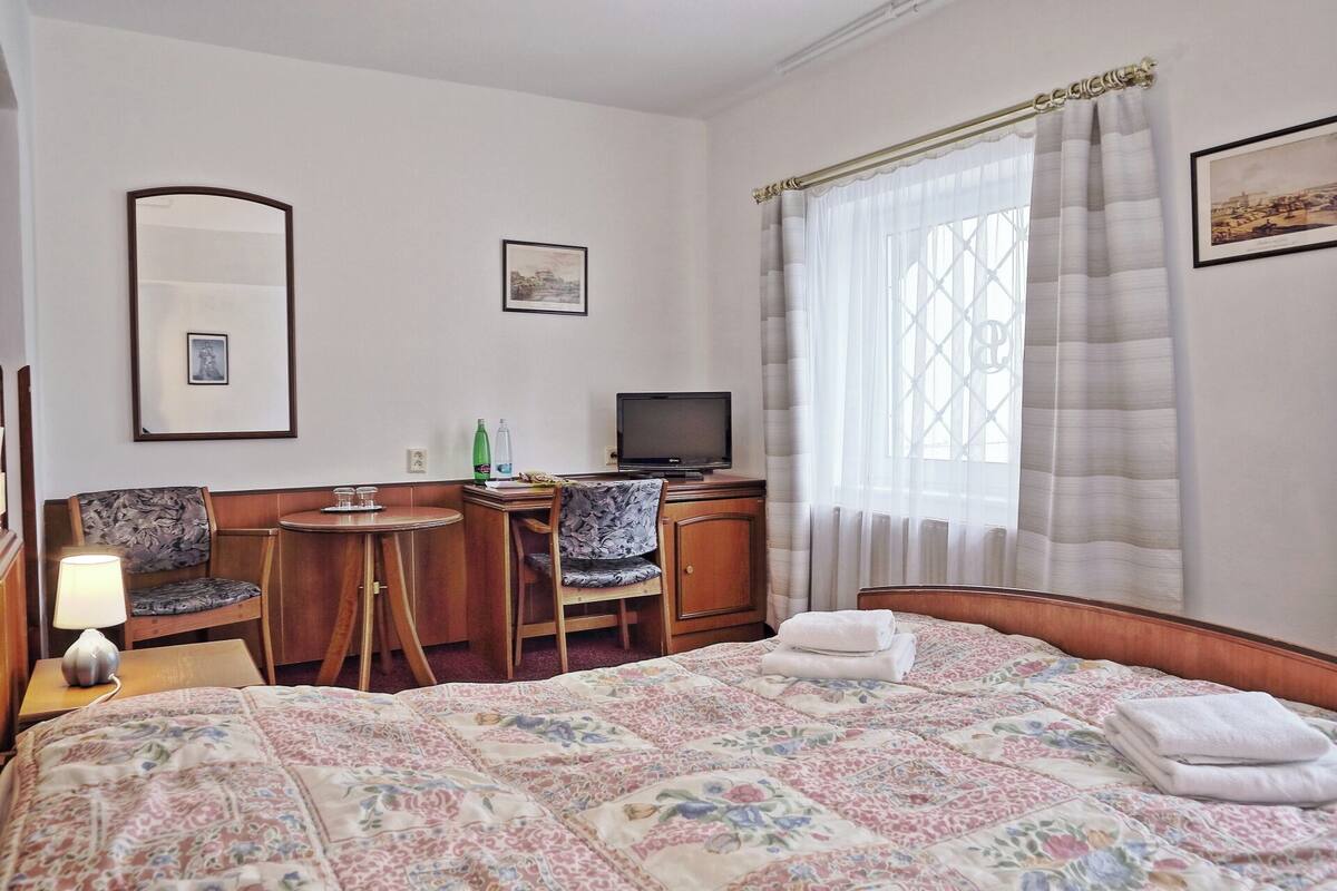 Une chambre d’hôtel avec un lit, un bureau équipé d’un ordinateur, une chaise, une lampe et une fenêtre avec des rideaux.