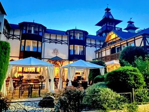 A building with a tower, a covered outdoor seating area, and a garden.