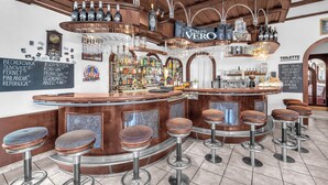 Eine Bar mit Holztresen, Hockstühlen und einer Auswahl an Flaschen und Gläsern.