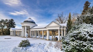 Ein großes, klassizistisches Gebäude mit einer zentralen Kuppel und zahlreichen Säulen, umgeben von schneebedeckten Bäumen.