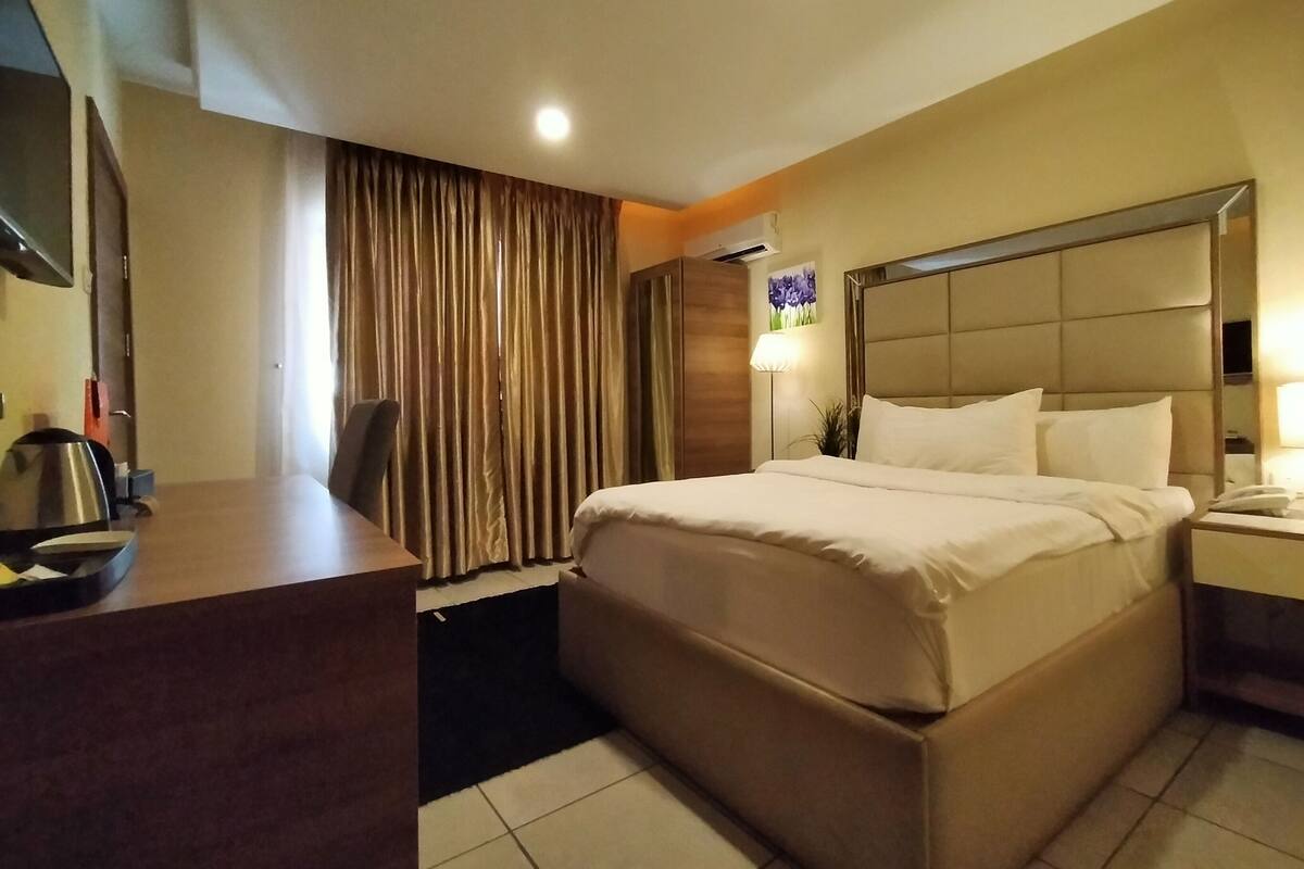 A hotel room with a bed, a desk, a chair, a TV, and a window with curtains.