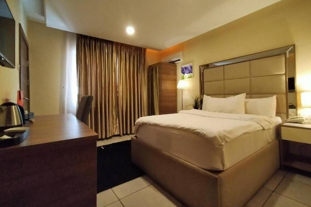 A hotel room with a bed, a desk, a chair, a television, and a window with curtains.