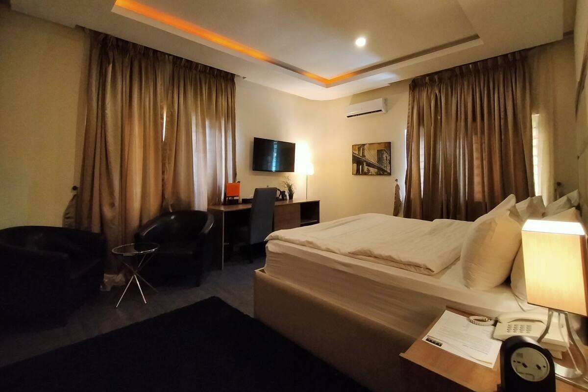 A hotel room with a bed, desk, chair, TV, and curtains.