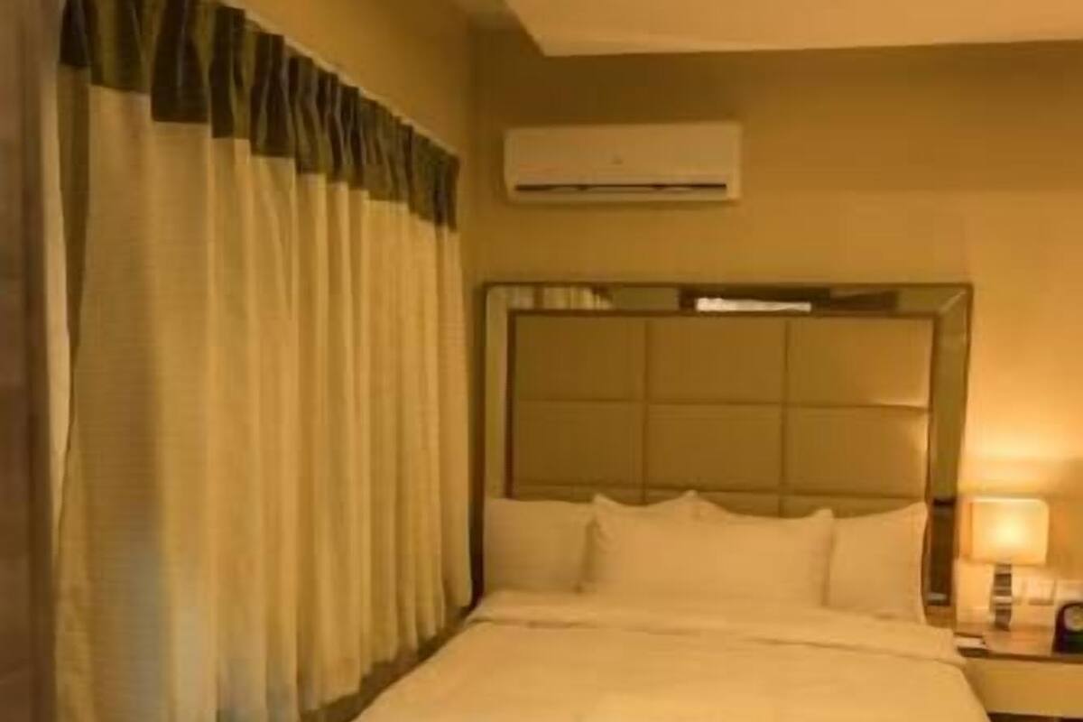 A hotel room with a bed, a chair, a nightstand, and an air conditioning unit.