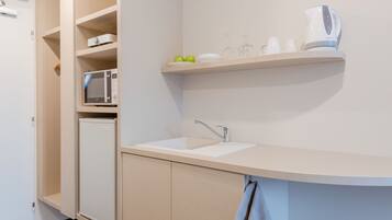 A compact kitchen with a microwave, a sink, and a kettle on a shelf.