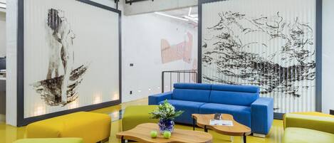 Un interior moderno con un sofá azul, sillas amarillas y verdes, y obras de arte en las paredes.