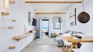 A modern interior with a wooden dining table, white chairs, a grey sofa, and a view to the outside. - Chrysalis Boutique Hotel (Astypalaia)