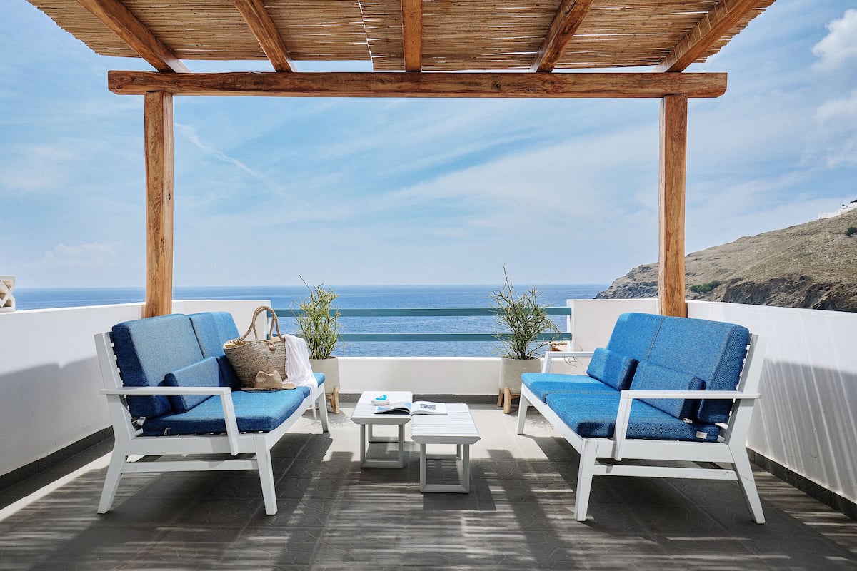 Una terraza con dos sillones azules acolchados, una mesita y una pérgola de madera.