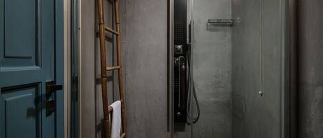 Ducha con cerramiento de vidrio, una escalera de madera y una toalla colgada en la pared, además de una lámpara.