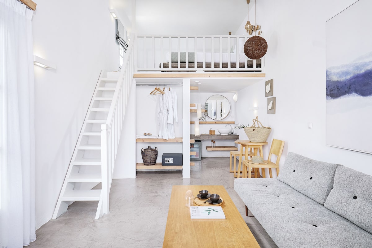 Un espacio habitable moderno y bien iluminado con un entrepiso de dormitorio, una zona de comedor y un sofá gris.
