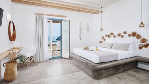 A modern bedroom with a bed, a desk, and a view of the sea through an open door. - Chrysalis Boutique Hotel (Astypalaia)