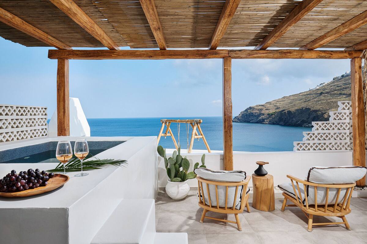 Una terraza con una pérgola de madera, muebles blancos, una planta de cactus y vistas al mar.