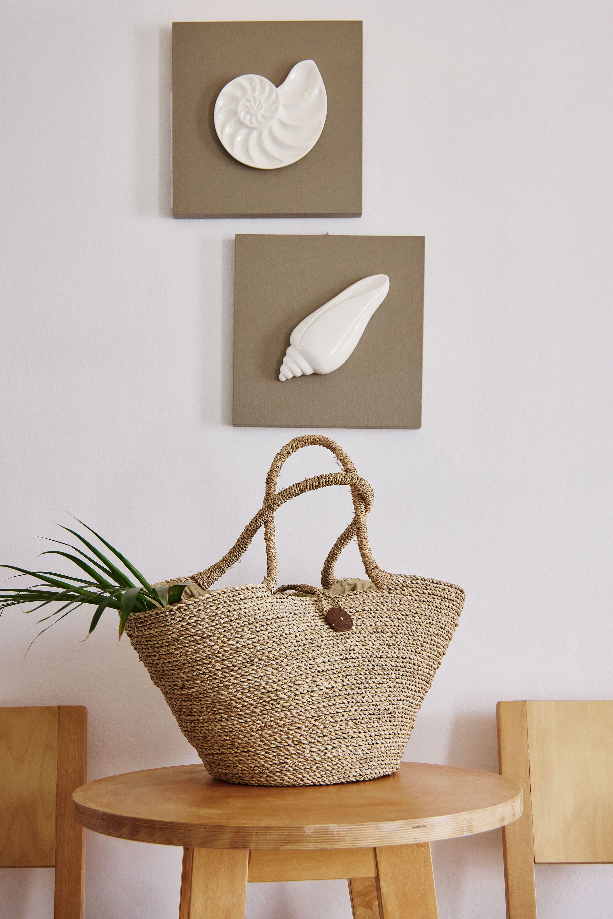 A woven basket with a handle on a wooden table against a wall with two framed white objects.